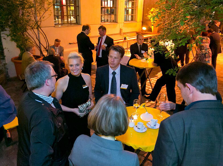Veranstaltungsgäste an gelben Stehtischen im begrünten Innenhof