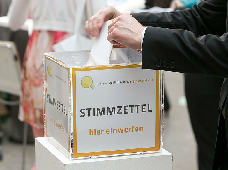 Hände stecken Stimmzettel in Wahlurne