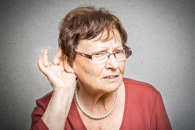 Frau hält sich die Hand ans Ohr um zu signalisieren, dass sie schwer hören kann