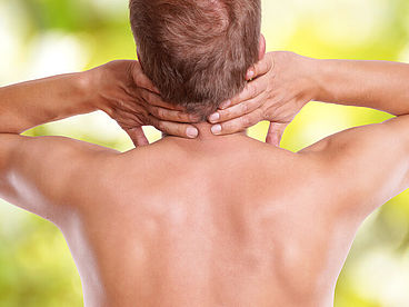 Ein Mann hält seine beiden Hände in den Nacken. Im Bereich der Halswirbelsäule kommt es durch einen Bandscheibenvorfall oft zu starken Schmerzen.  