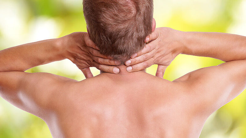 Ein Mann hält seine beiden Hände in den Nacken. Im Bereich der Halswirbelsäule kommt es durch einen Bandscheibenvorfall oft zu starken Schmerzen.  