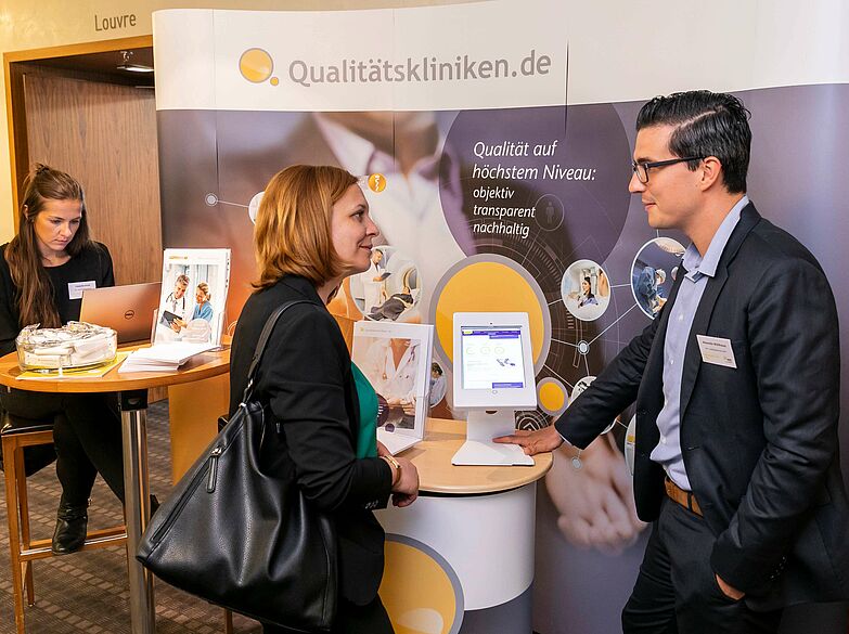 Beratungsgespräch zwischen einem Mitarbeiter von Qualitätskliniken.de und einer interessierten Besucherin am Messestand von Qualitätskliniken.de. 
