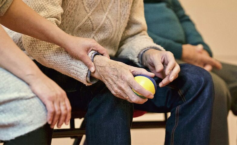 Pflegende unterstützt Patienten dabei einen Ball zu greifen.