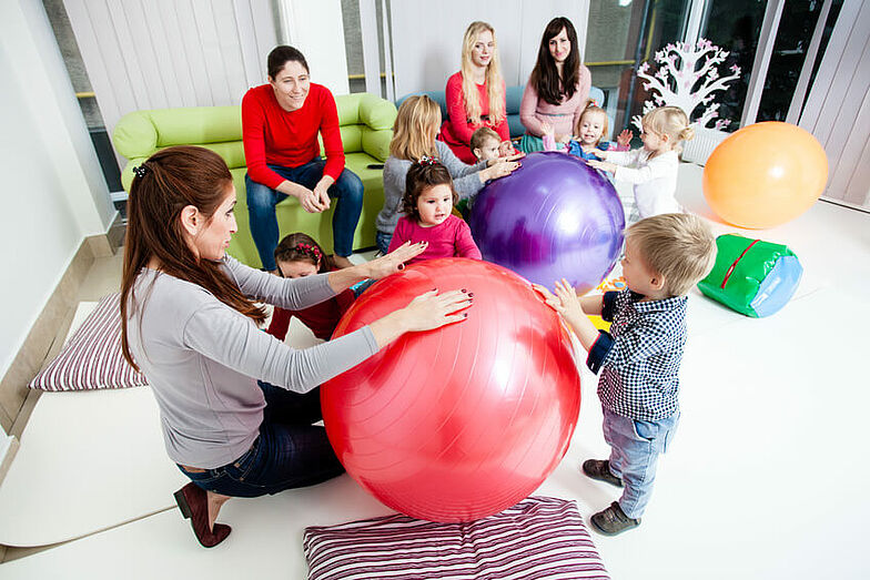 Mehrere Mütter mit ihren Kindern spielen zusammen mit Gymnastikbällen.