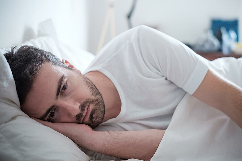 Ein Mann liegt nachdenklich im Bett. Die Anzeichen einer Depression sind vielfältig. Auch Schlafstörungen und ein pessimistischer Zukunftsblick sind Charakteristika für eine Depression.