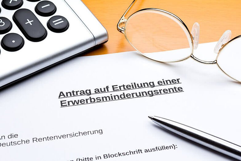 Ein Antrag auf Erteilung einer Erwerbsminderungsrente liegt zusammen mit einem Kugelschreiber, einem Taschenrechner und einer Brille auf einem Tisch.