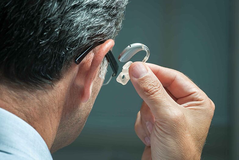 Mann mit Brille setzt sich ein Hörgerät in das rechte Ohr.