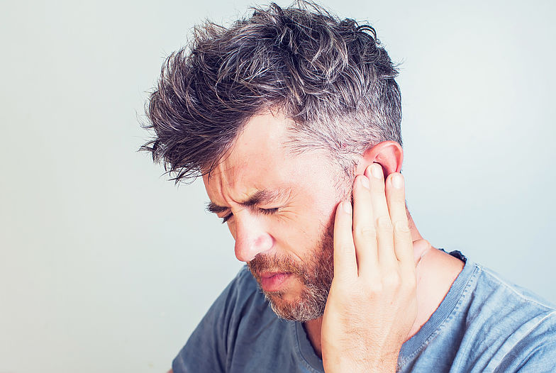 Mann hält sich das linke Ohr mit seiner Hand aufgrund eines Tinnituses.