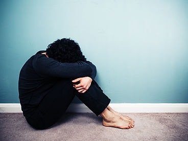 Mann mit einer posttraumatischen Belastungsstörung sitzt zusammengekauert auf dem Boden.