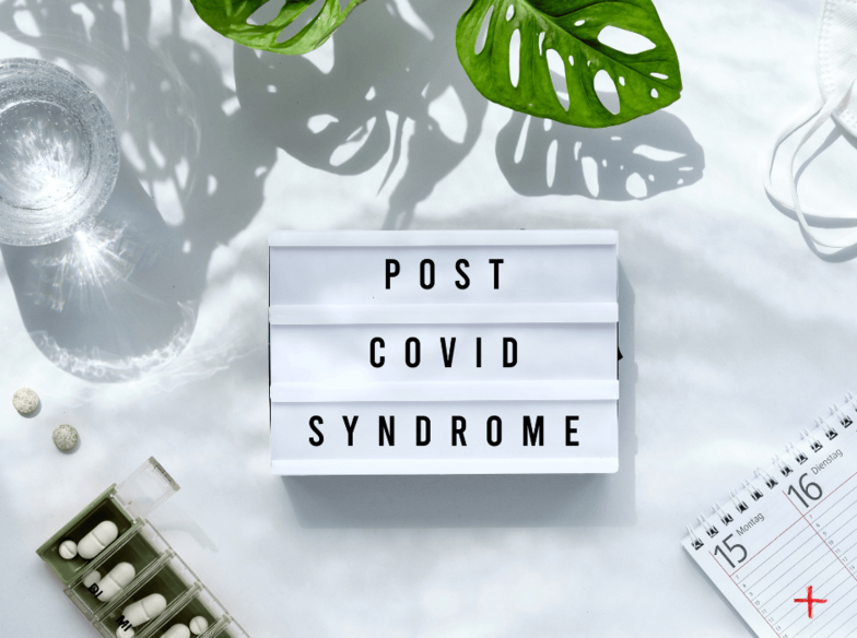 Schriftzug Post Covid Syndrome auf weißem Hintergrund mit Medikamenten, Wasserglas, Kalender.