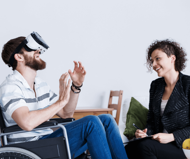 Patient im Rollstuhl mit VR-Brille und Therapeutin daneben.