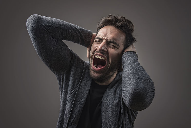 Ein Mann leidet an Anpassungsstörung und hält sich vor lauter Lärm die Ohren zu, während er schreit, da es kaum erträglich ist.