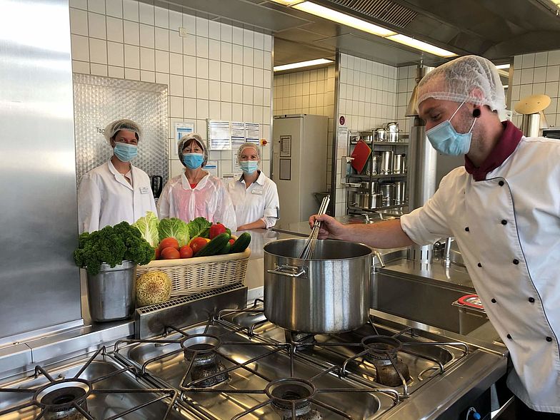 Küchenleiter mit Team am Kochtopf in Klinik-Großküche