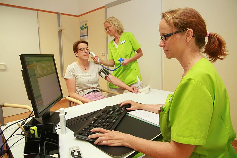 Mitarbeiterinnen untersuchen eine Patientin unfd dokumentieren die Ergebnisse