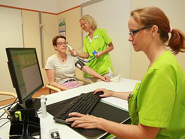 Mitarbeiterinnen untersuchen eine Patientin unfd dokumentieren die Ergebnisse