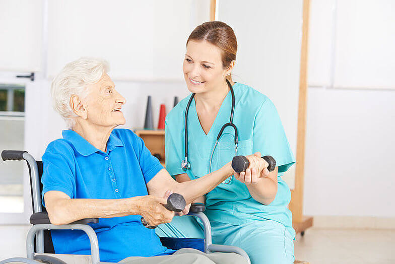Pflegende kümmert sich um geriatrische Patientin im Rollstuhl.