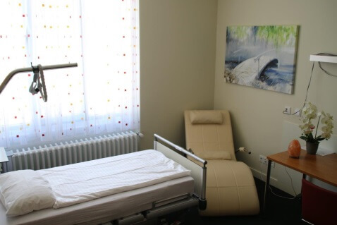 Patientenbett vor hellem Fenster und wohnlicher Dekoration